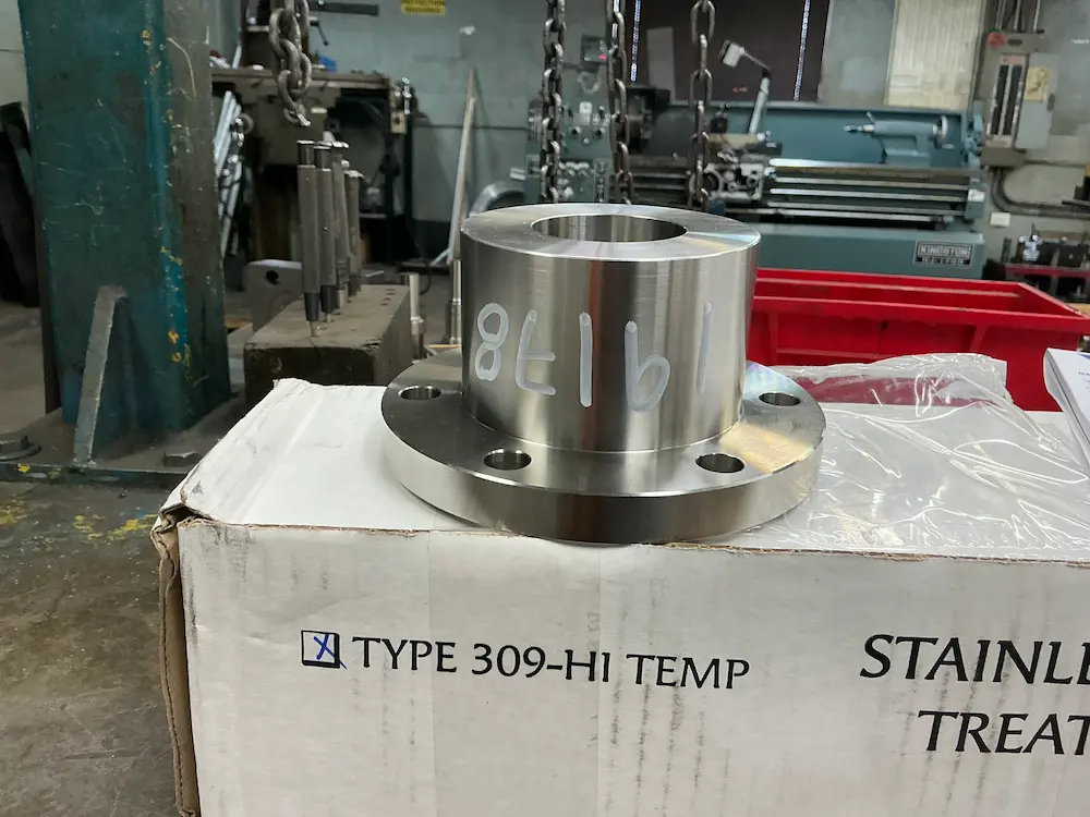 Side-angle view of a precision-machined stainless steel pipe flange resting on a shipping box.