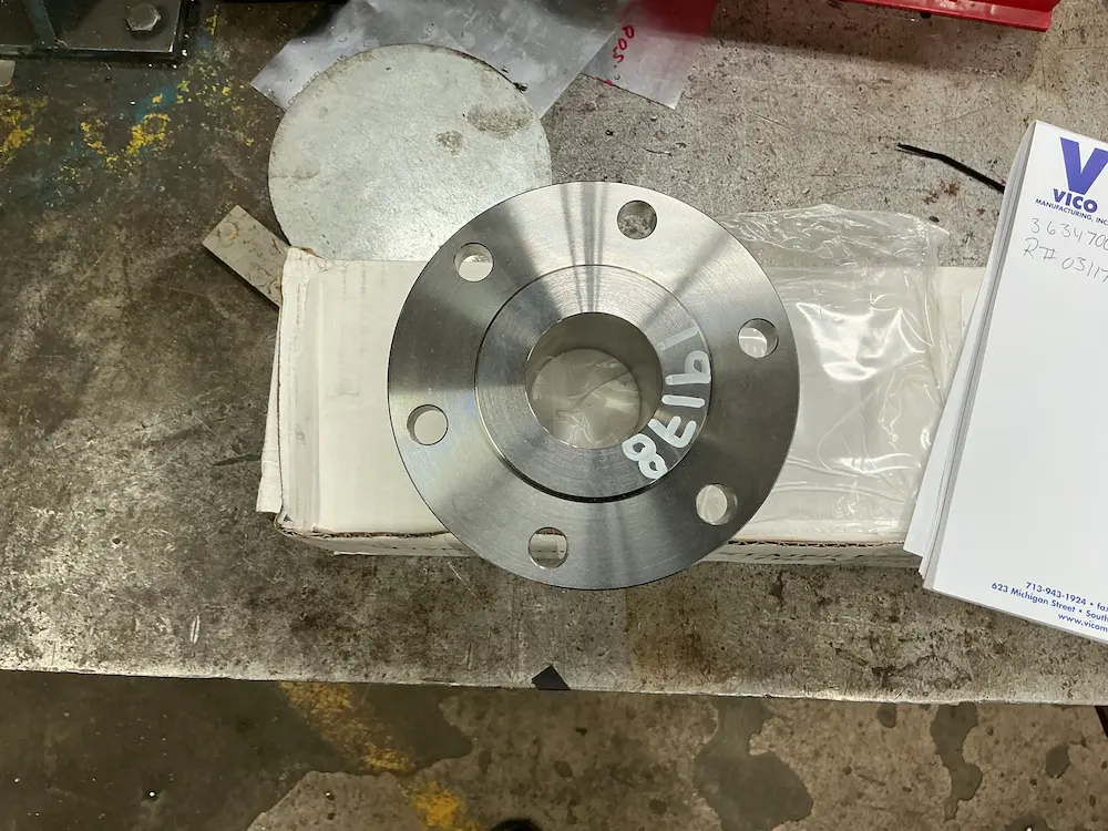 Top-down perspective of a precision Wire EDM machined stainless steel flange face with part markings.